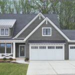 This two-story home has grey engineered shingle siding with white trim. There are two attached garages with white garage doors.