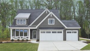 This two-story home has grey engineered shingle siding with white trim. There are two attached garages with white garage doors. 