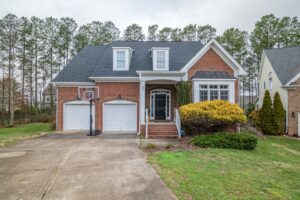 A two-story brick home with a two-car garage. There is a basketball hoop outside on the paved driveway.