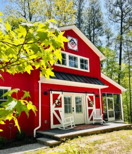 A red home with metal siding and white trim has two white rocking chairs on the porch.