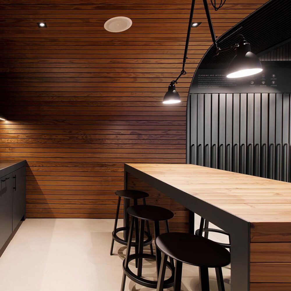 This picture depicts a kitchen with pine paneling incorporated throughout the space. There are bar stools pulled up to a counter with hanging light fixtures placed above the counter.