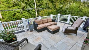 A deck with black and brown patio furniture, white railings, and gray porcelain tiles. 