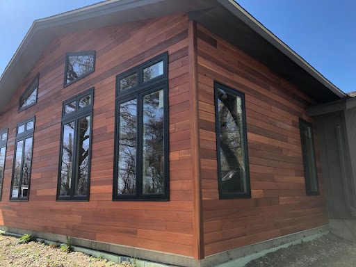 The picture depicts the exterior corner of a cabin-style house. There are long windows with black framing.